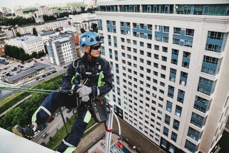 Industrial mountaineering worker in uniform hangs over construction building